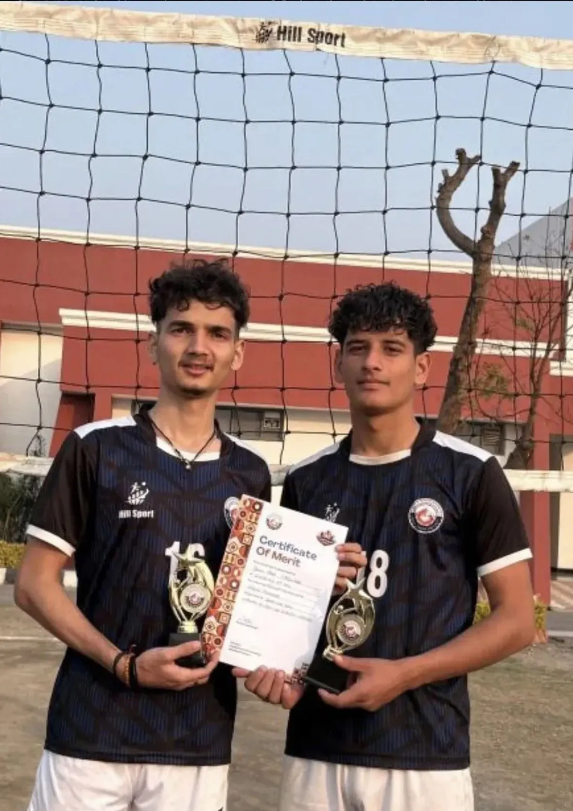 Two GEHU volleyball players holding trophies and a certificate of merit